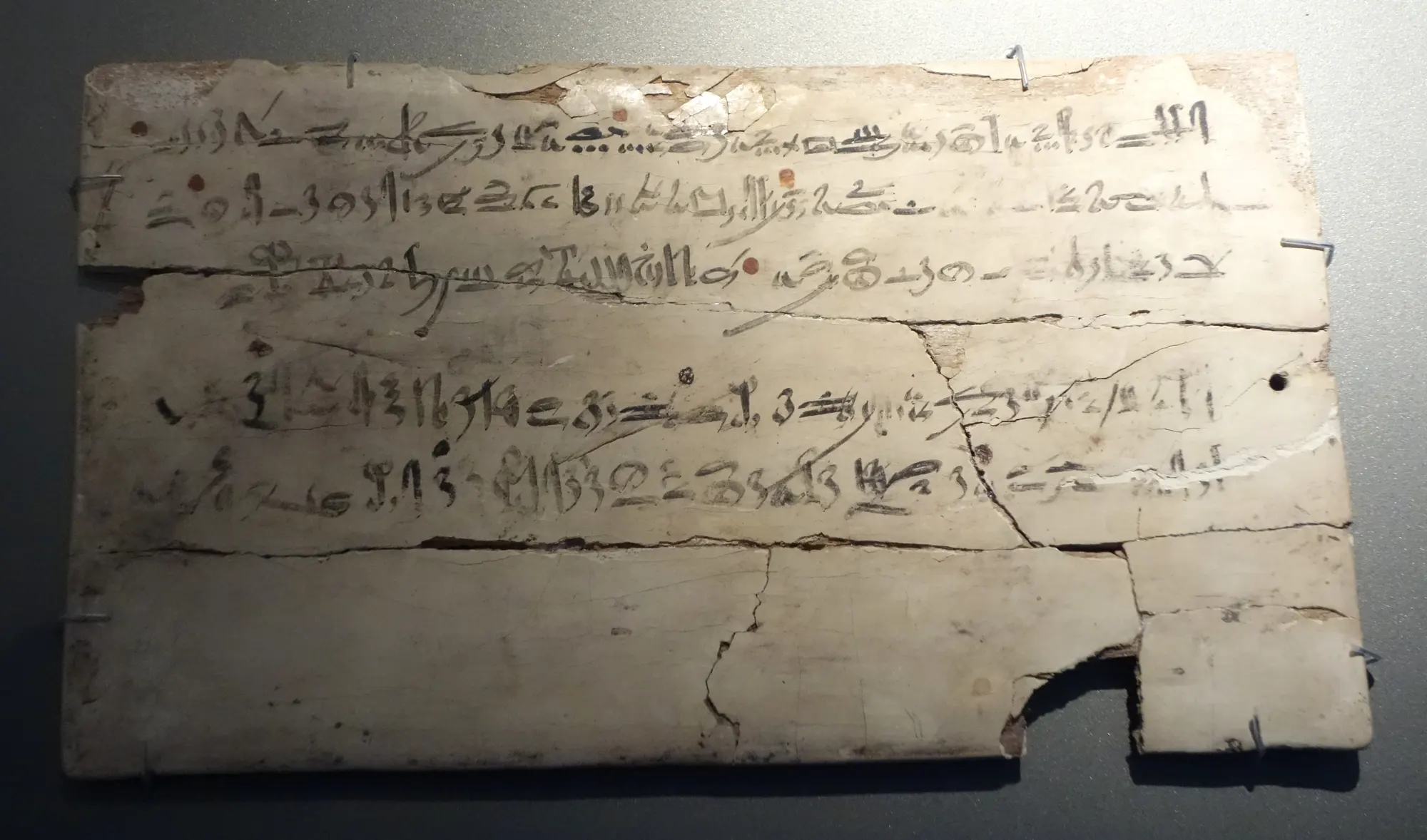 Scribe's board, Dynasty 18: rows of black hieratic script with a few red marks, cracked across the lower half