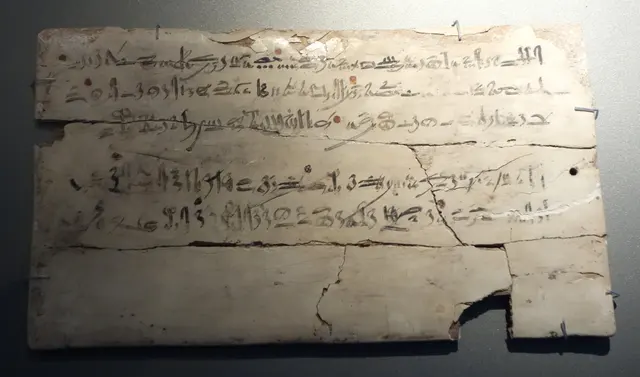 Scribe's board, Dynasty 18: rows of black hieratic script with a few red marks, cracked across the lower half