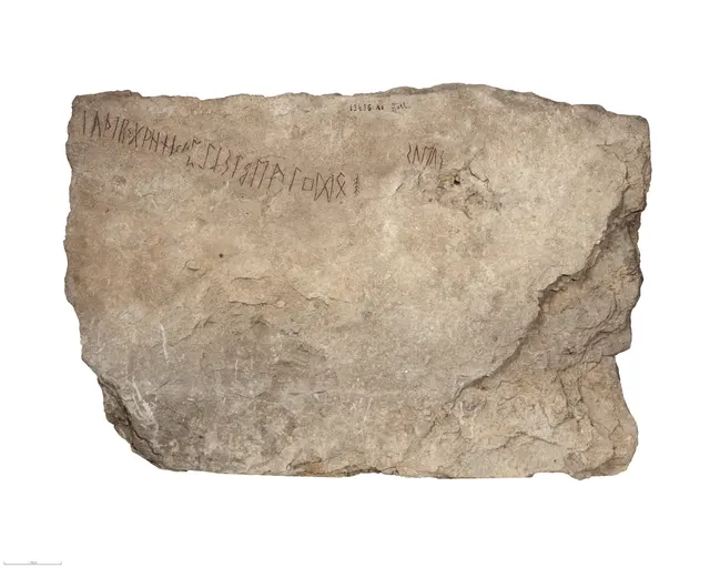Gray limestone slab with a line of runes along its upper edge and a short word at upper right