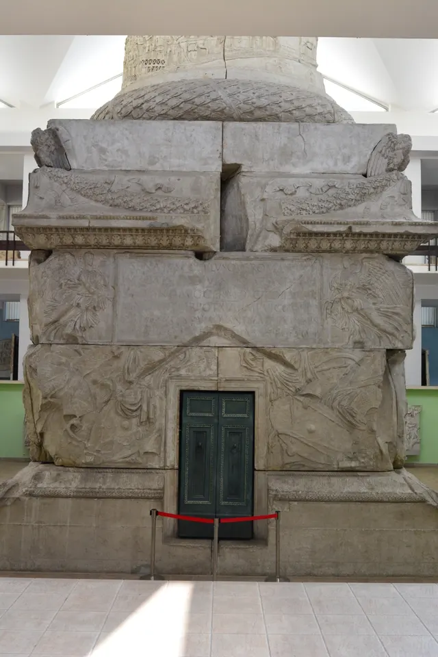 Photo: plaster cast of the base of Trajan's Column, Bucharest; Latin inscription panel above a door, winged figures beside it